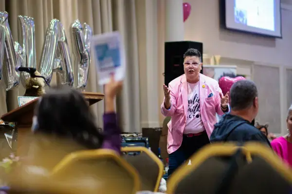 Auctioneer in pink jacket turns their attention to a bid at an auction
